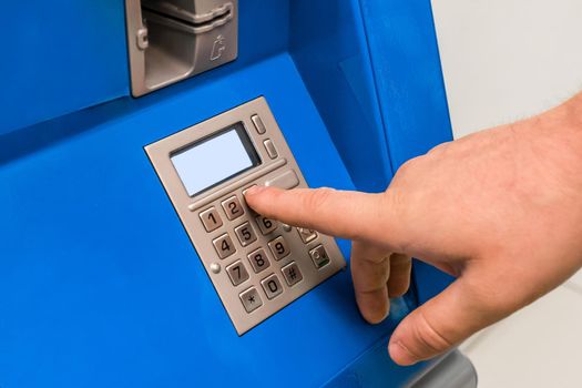 A man's hand dials a pincode at the terminal for issuing money, close-up.