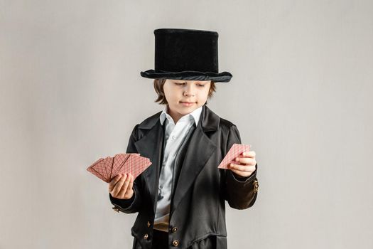 Young six year old boy wearing black suit and showing playing cards trick during illusionist performance. Cosplay, Retro party or Halloween costume concept.