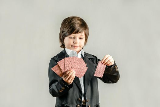 Young six year old boy wearing black suit and showing playing cards trick during illusionist performance. Pocker player