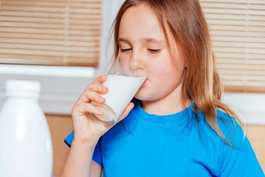 Cute little girl is drinking milk indoors