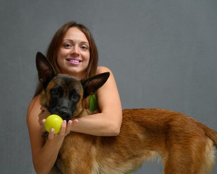 Portrait woman posing with ball smiling with belgian shepherd malinois sitting on floor in studio