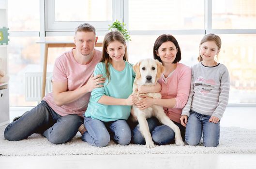 Happy family with dog sitting on floor in light room