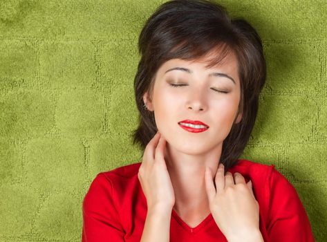 Young woman lying with eyes closed on a green background, space for text