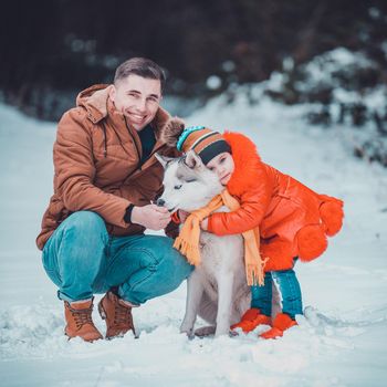 Happy father with daughter on a walk in the woods, girl and husky in yellow scarves, bright clothes in winter.2021