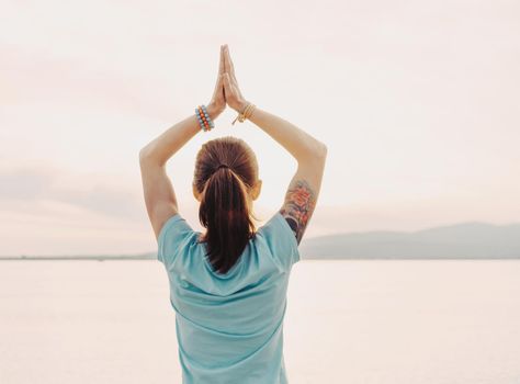 Young woman doing yoga and meditating on background of sea, hands in praying gesture.
