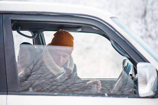 Traveler young man sitting with cup of hot drink in car in winter.