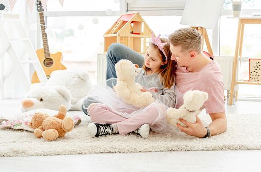 Cute little princess playing with teddy bears with smiling father in children's room