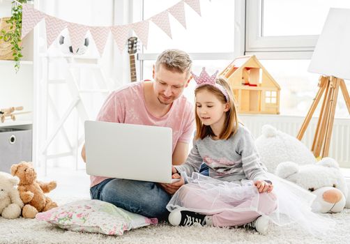 Handsome father teaching pretty daughter to work on laptop in children room