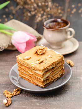 Slice of layered honey cake on a plate with cup of coffee and tulip flower, selective focus