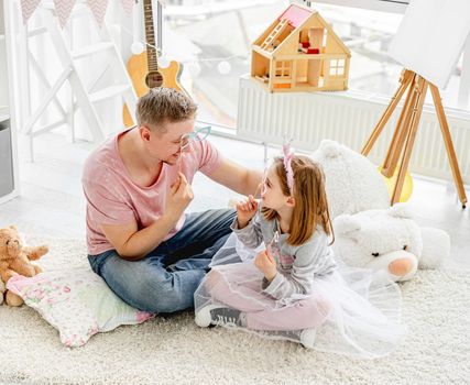 Smiling man and happy girl fooling with glasses on stick indoors