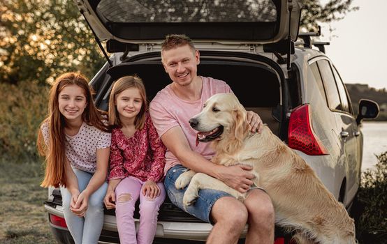Family with golden retriever dog next to open car trunk on nature at sunset