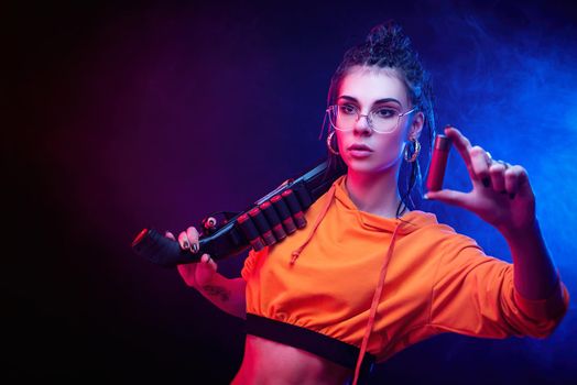 a sexy brunette in an orange jumpsuit with a shotgun on a dark background in neon light