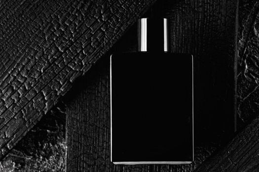This is a promotional photo of eau de toilette or perfume in a dark style. Black bottle on the background of a burnt tree. Layout for logo or sale information or Black Friday.