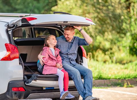 Father with daughter sitting on car trunk after schooling