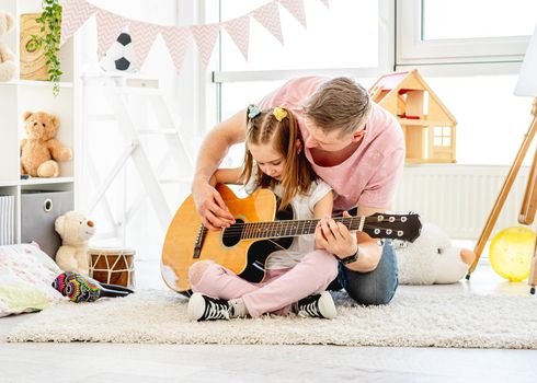 Handsome father playing guitar with cute daughter in beautiful room