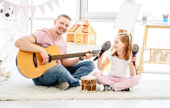 Smiling father and little daughter playing musical instruments in kids room