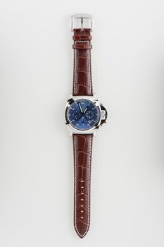 luxury fashion watch with blue dial and brown crocodile grain leather watch band on white background