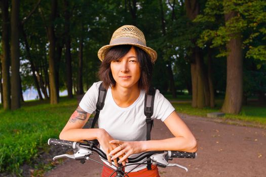Young woman hipster standing with a bike in a summer park