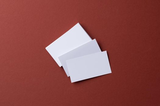 Blank white business cards on burgundy paper background, top view