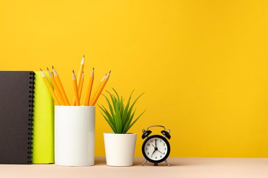 Cup of pencils and notepads on desk against yellow background, front view