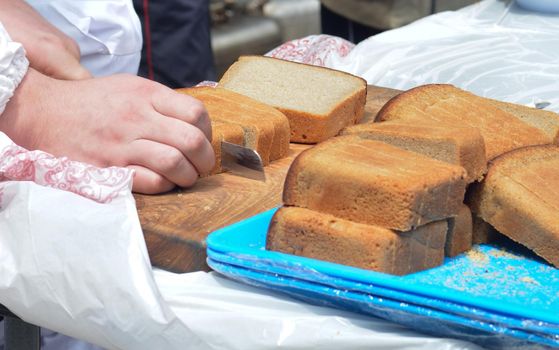 Male hands cutting rye bread on the wooden board