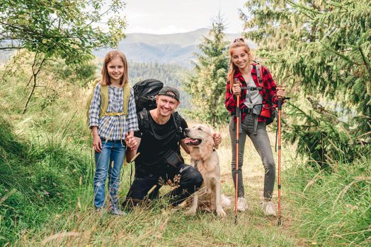 Smiling father with daughters and dog hiking sunny mountain