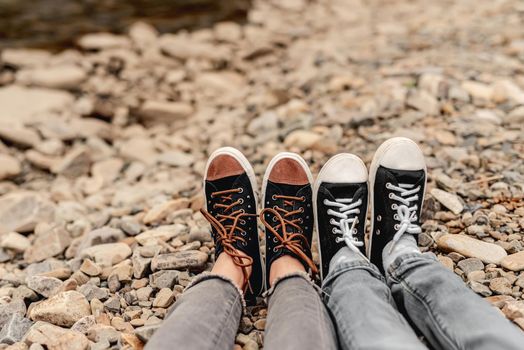 Two pairs of legs in black gumshoes resting on stones outdoors