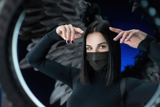 the brunette woman on a background of black wings in a protective mask against coronavirus with hands portrait