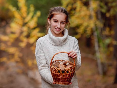 Teenage girl holding wicker basket with edible mushrooms standing on autumn forest background