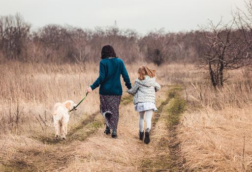 Mother and daughter walking dog along dirt road