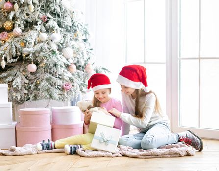 Smiling sisters in santa hats opening new year gifts