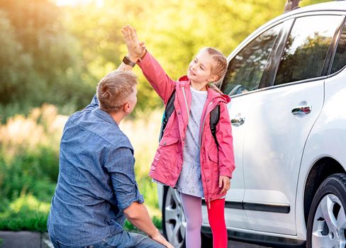 Little girl greeting father after school near car on sunny nature background
