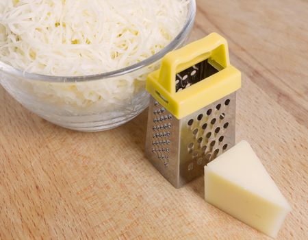 Grated cheese in a bowl, small grater, small piece of cheese on a wooden table