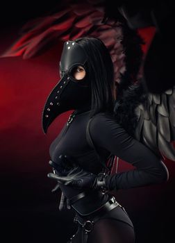the woman wearing a plague doctor mask with leather straps and black wings on a dark red background