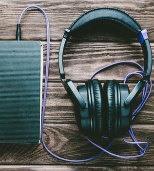 Headphones with a paper book on a wooden background, top view. Concept of audiobook.