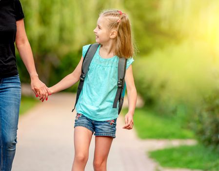 Little schooler walking hand in hand with mother in sunny park