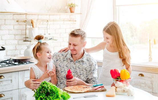 dad with two little daughters preparing pizza in the kitchen