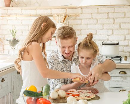 dad with two little daughters preparing pizza in the kitchen