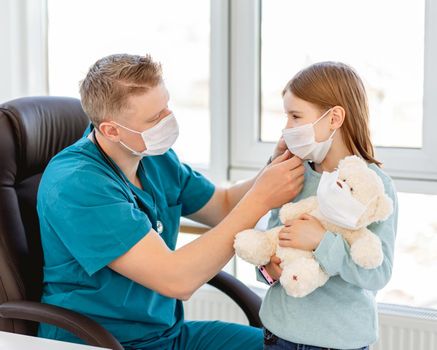 Kind doctor putting medical mask on little girl in clinic