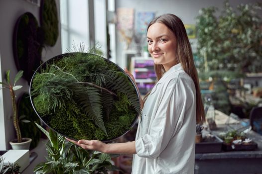 Confident female florist is holding a plant composition in her own flower and plants shop