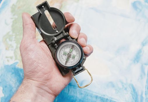 Male hand with travel compass on background of map.