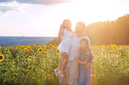 daddy with little daughters at sunset in sunflower field