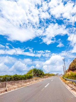 Dry asphalt empty automobile road with concrete barrier and marking lines on a sunny summer day with blue cloudy sky. Car travel trip concept background. Stories vertical format.