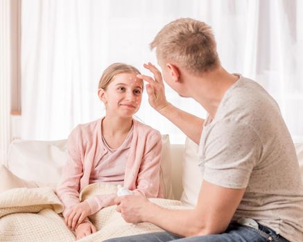 Good father puts special medicine on daughters rash, caused by chickenpox