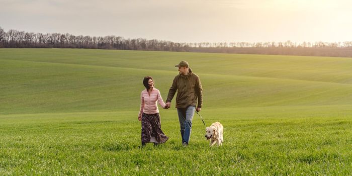 Lovely couple walking cute dog on spring field