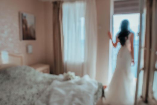 Blurred image for the background. Back view of beautiful brunette bride young woman in the white lace dress near window in the hotel room. Wedding concept