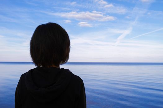 Young woman admires the lake, thinking about life, view from the back