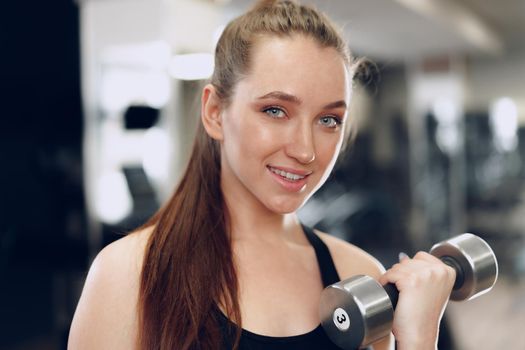 Young brunette sporty woman exercising with dumbbell in a gym close up