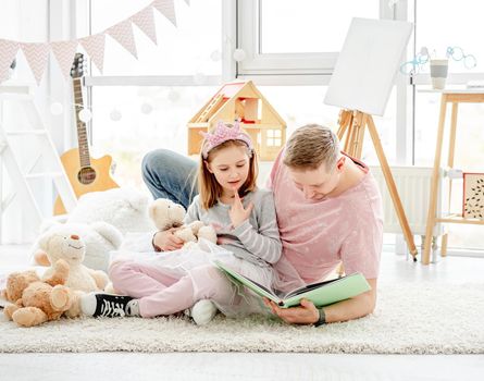 Cute little daughter with happy father reading book