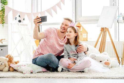 Happy father with cute daughter taking selfie in kids room